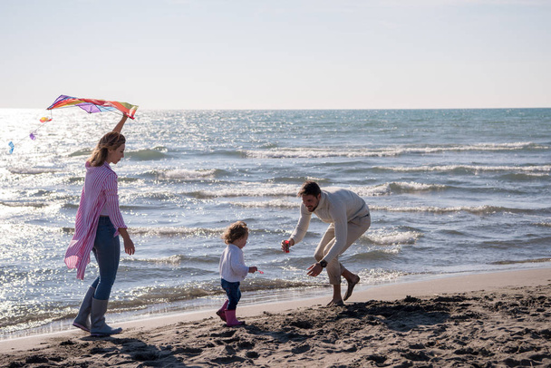 Genç bir aile, çocukları dinleniyor ve sonbahar günü kumsalda uçurtmayla eğleniyorlar. - Fotoğraf, Görsel