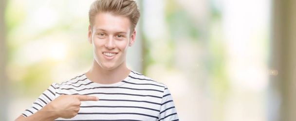 Jeune homme blond beau portant des rayures marin t-shirt avec visage surprise pointant du doigt vers lui-même
 - Photo, image
