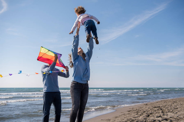 young family with kids resting and having fun with a kite at beach during autumn day - Photo, image