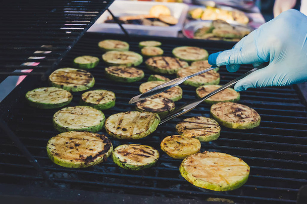 Contrast grill grid with fried zucchini. Cook in a clean glove flips to the other side of the fried zucchini. The process of cooking vegetables on the grill. - Photo, Image