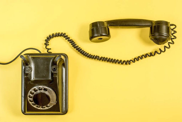 Teléfono negro vintage con auriculares y cable enrollado sobre fondo amarillo
 - Foto, Imagen
