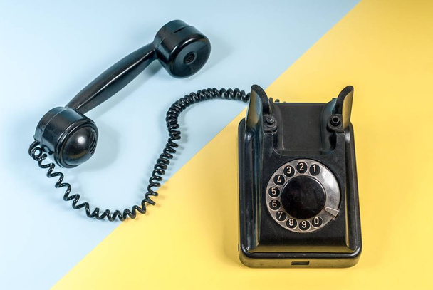 Vintage black telephone with a headset and coiled cable on blue and yellow - Foto, immagini