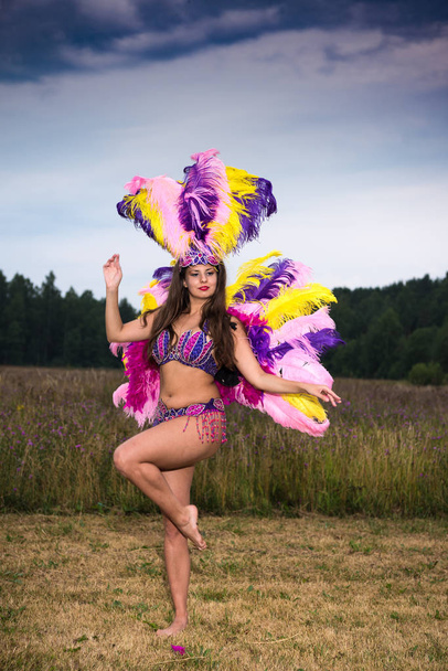 Young girl in bright colorful carnival costume posing outdoors at sunset. Sexy brunette preparing for carnaval - Photo, Image