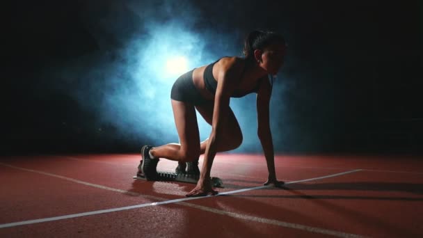 Koşu ayakkabıları sprint spor ayakkabı içinde stadyumun parça koyu arka plan üzerinde çalıştırmak için profesyonel kadın atlet karanlık bir arka plan üzerinde - Video, Çekim