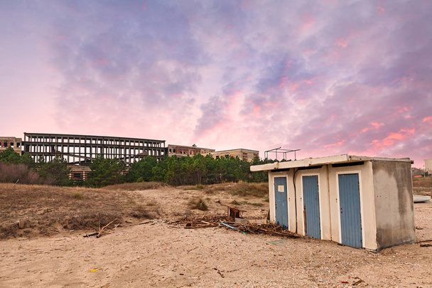 puesta de sol en la playa con cabaña abandonada y ruinas de un antiguo edificio en el fondo - paisaje triste y desolado bajo un cielo nublado dramático
 - Foto, imagen
