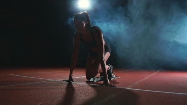 Atletka na tmavém pozadí se chystá spustit běžecké sprint z podložky na běžeckém pásu na tmavém pozadí - Záběry, video