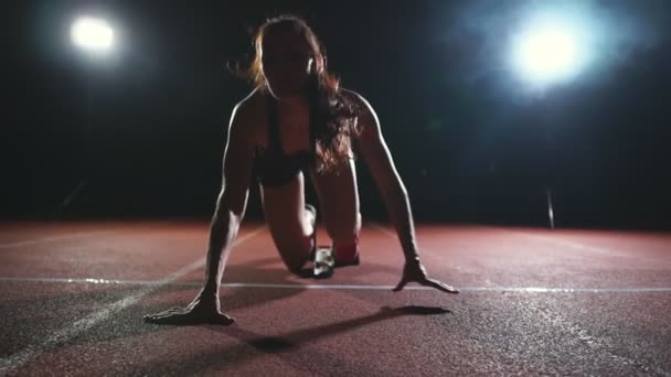 Professionele vrouw atleet op een donkere achtergrond gotovtes uit te voeren van de sprint van Jogging schoenen in sneakers op het spoor van het stadion op een donkere achtergrond. Close-up - Video