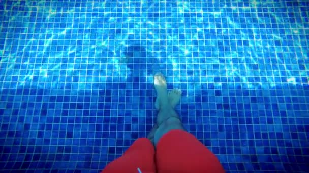 Der nackte Fuß des Mannes entspannt sich im strahlend blauen Swimmingpool, der unter Wasser glitzert. Wasser mit Sonnenreflexion, Urlaub, Entspannung, Ausflugskonzept - Filmmaterial, Video