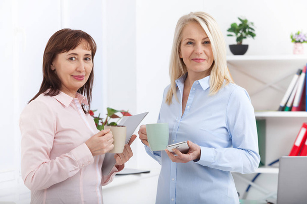 Office coffee break. Two female colleagues with cups of coffee talking in offise. - Fotoğraf, Görsel