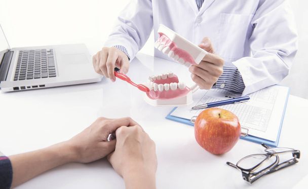 Dentista Mostrando limpieza de dientes cepillo dentadura postiza o modelo de mandíbula dental, instrumentos de odontología en el consultorio del dentista
. - Foto, imagen