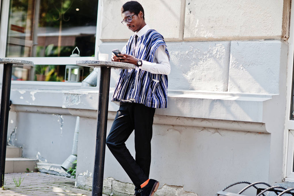 African man in traditional clothes and glasses at outdoor caffe, drink coffee and looking daily news on phone. - Foto, Bild