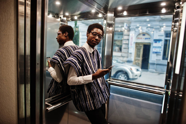 African man in traditional clothes and glasses with mobile phone at elavator or modern lift. - Foto, Imagen