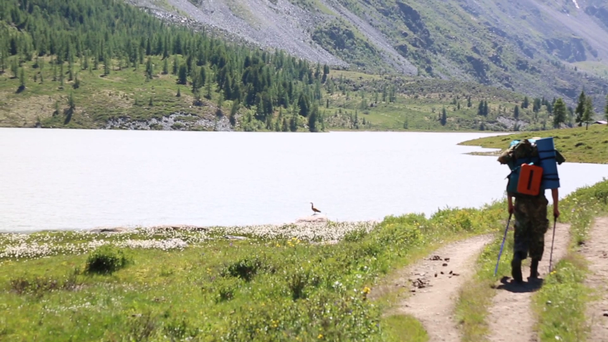 Un uomo con uno zaino cammina lungo un fiume di montagna. Un turista con una grande borsa sulla schiena cammina lungo le rocce vicino a un rumoroso fiume veloce
. - Filmati, video
