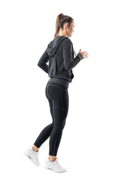 Rear side view of sporty female jogger jogging in hooded sweatshirt and leggings. Full body length portrait isolated on white background. - Foto, Bild