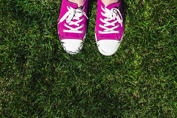 Jambes en vieilles baskets roses sur herbe verte. Vue d'en haut. Le concept de jeunesse, de printemps et de liberté
. - Photo, image