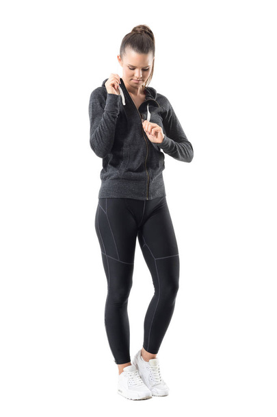 Aktiv fitte Sportlerin, die das Kapuzenpullover-Sweatshirt mit Reißverschluss auszieht und nach unten schaut. Ganzkörperporträt isoliert auf weißem Hintergrund. - Foto, Bild