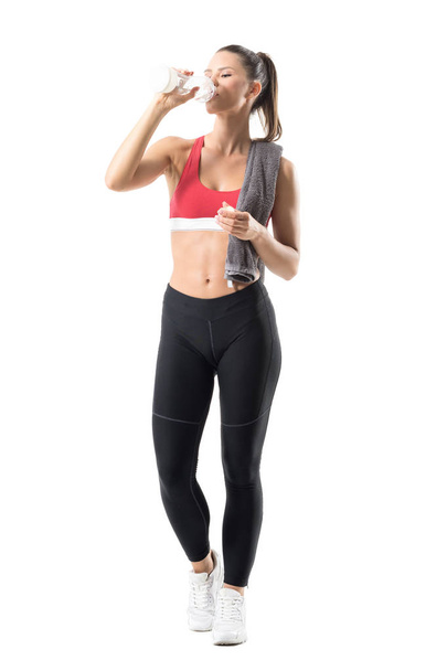 Front view of tired young sportswoman runner drinking water with head titled back. Full body length portrait isolated on white background. - Foto, afbeelding