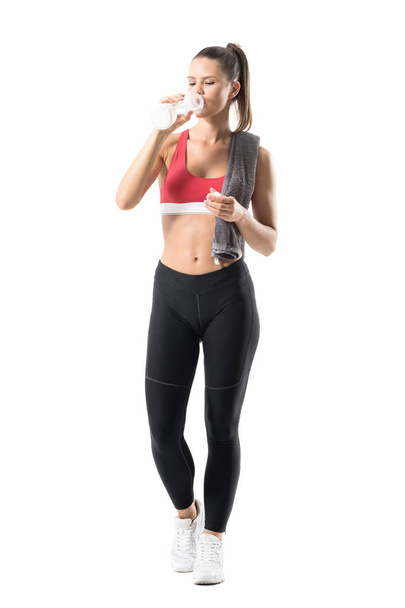 Front view of thirsty young sporty woman drinking water from glass bottle. Full body length portrait isolated on white background. - Zdjęcie, obraz