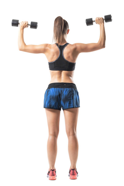 Back view of gym woman doing shoulders and back exercise with weights. Lower arm position. Full body length portrait isolated on white background. - 写真・画像