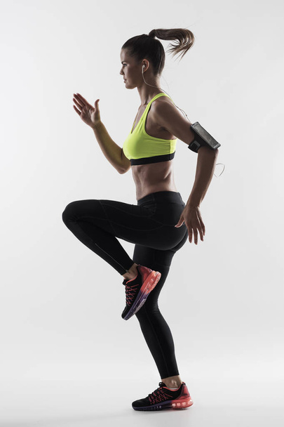 Silueta desaturada retroiluminada de mujer atlética corredor movimiento mientras corre rápido sobre fondo gris estudio
. - Foto, Imagen