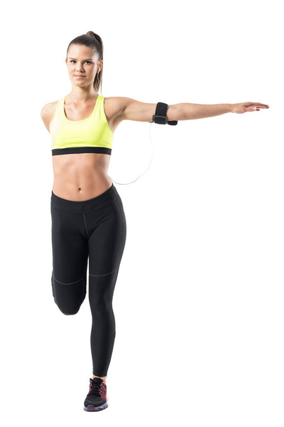 Pretty female sporty jogger stretching leg and arm balance exercise. Full body length portrait isolated on white studio background - Photo, Image