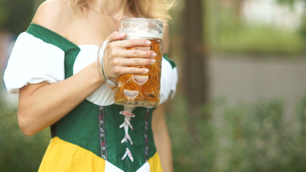 Close-up de um copo de cerveja bávara nas mãos de uma jovem garçonete vestida com roupas nacionais. Festivais de música e cerveja Oktoberfest
 - Filmagem, Vídeo