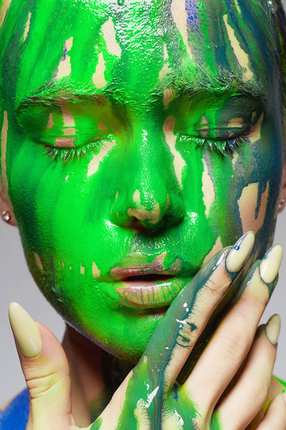 Jonge vrouw in groene verf. vloeibare verf stroomt over een mooi gezicht en lichaam. Kleur close-up portret van meisje in verf - Foto, afbeelding