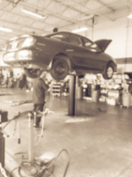 Винтажный тон размыл абстрактного механика, осматривающего поднятый автомобиль в автомастерской в Техасе, США. Рабочий техник в гараже
 - Фото, изображение