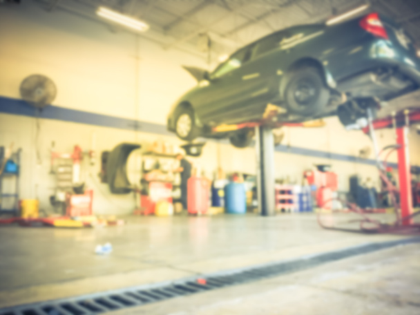 Motion blurred abstract mechanic changing oil below lifted car at auto shop in Texas, USA. Defocused background interior of modern oil change service station. Working technician at garage concept - Photo, Image