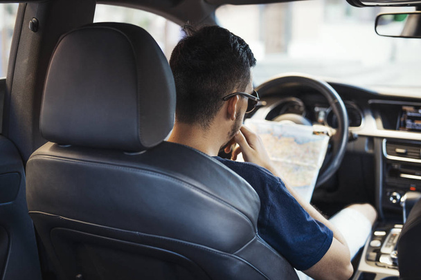Close up of young man looking at map behind the wheel in car. - Photo, image