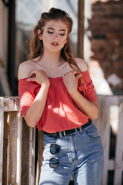 Mooie jonge vrouw in jeans en rode t-shirt poseren in studio  - Foto, afbeelding