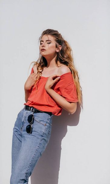 Mooie jonge vrouw in jeans en rode t-shirt poseren in studio  - Foto, afbeelding