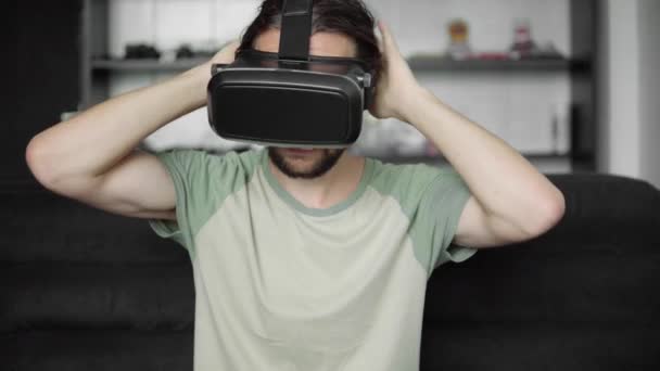 Young bearded hipster man start using his VR headset display for virtual reality game or watching the 360 video while sitting on sofa at home in the living room. VR Technology. - Video