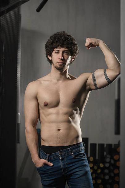 Portrait attractive sexy narcissistic shirtless guy demonstrating his biceps in gym - 写真・画像