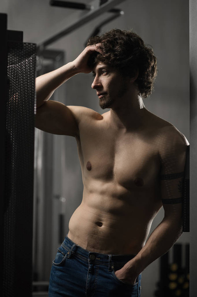 Joven hombre atractivo descansando en el gimnasio después de hacer ejercicio, posando masculino
 - Foto, Imagen