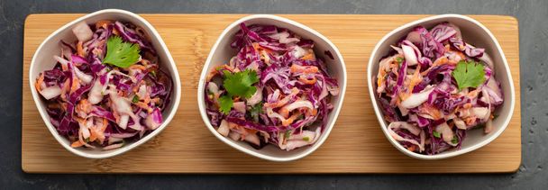 Фиолетовая капуста и морковный салат с майонезом в белой миске на черном фоне. Набор из трех классических салатов из капусты. Вегетарианское блюдо. Вид сверху
. - Фото, изображение