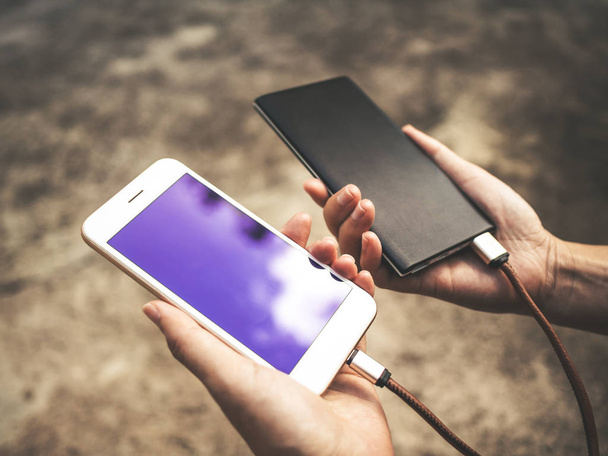 Human hands holding white smartphone charging battery from external power bank in outdoor - Photo, Image
