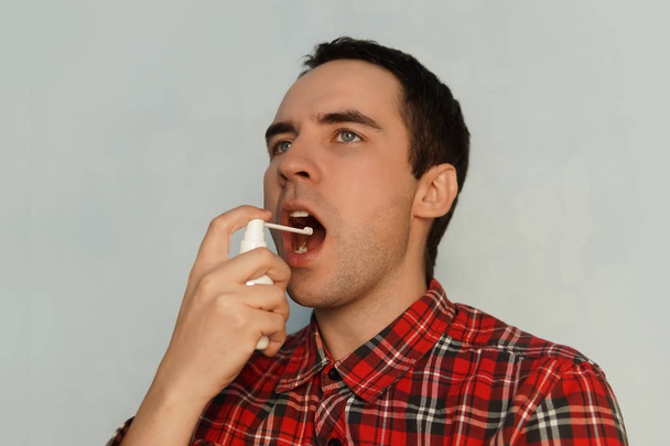 Hasta adam beyaz spreyin boğaz spreyini tedavi ediyor. Genç adam üşütmüş. Boğazdaki şişmiş bezlerin tedavisi için. Ferahlatıcı bir nefes. Nefesi kokuyor. mentollü - Fotoğraf, Görsel