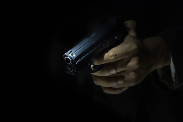 Крупним планом чоловіча рука тримає пістолет з темним фоном для показу текстів
 - Фото, зображення