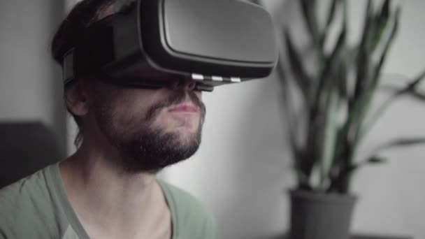 Nuori parrakas hipsteri mies käyttää hänen VR kuulokkeet näyttö katsomassa 360 video istuessaan sohvalla ja syö evästeitä kotona olohuoneessa. VR-teknologia
. - Materiaali, video