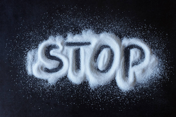 塩は、黒の表面に散在しています。描かれた単語を停止します。塩と砂糖の過剰摂取から健康に害を及ぼすのコンセプト - 健康食品、ダイエット、. - 写真・画像