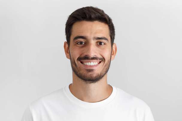 Close up portrait of smiling attractive man in white t-shirt isolated on gray background - Фото, зображення