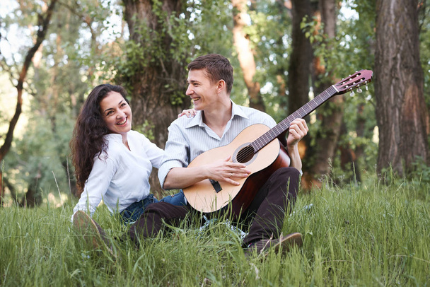 森の中に座っていると再生ギター、夏の自然、明るい日光の下の若いカップルは、影と緑の葉、恋愛感情 - 写真・画像