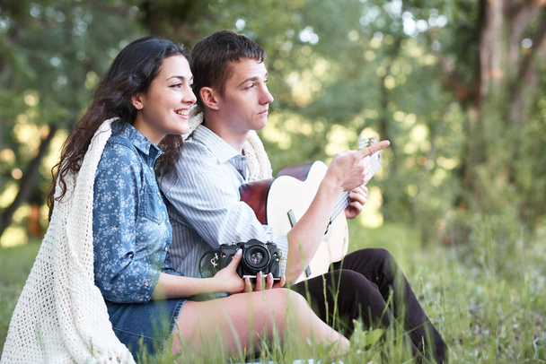 young couple sitting in the forest and playing guitar, summer nature, bright sunlight, shadows and green leaves, romantic feelings - Foto, afbeelding