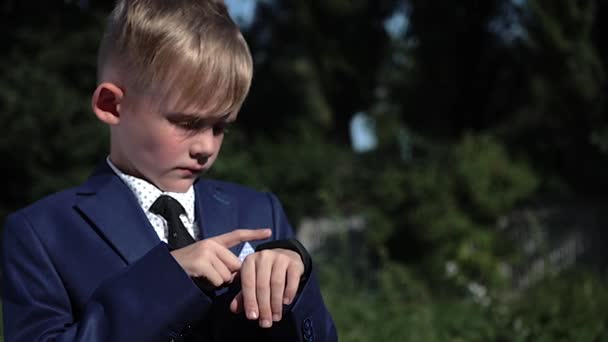 Chłopiec dziecko w garniturze użyć inteligentny zegarek na ulicy. Strzał z bliska - Materiał filmowy, wideo
