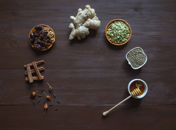 Zutaten auf dem braunen Tisch zum Backen mit Honig, Ingwer, Zimt, Nelken, Trockenfrüchten und Hanfsamen. - Foto, Bild