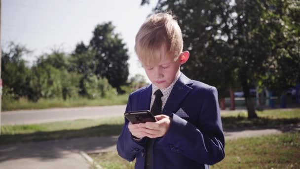 Kleiner Junge im Anzug hält Smartphone und spielt auf der Straße - Filmmaterial, Video