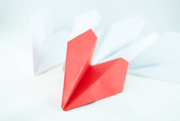 Red paper plane among white ones on a white background, isolated. Concept (idea) of airlines, freedom, leadership, success, and individualism. - Fotó, kép
