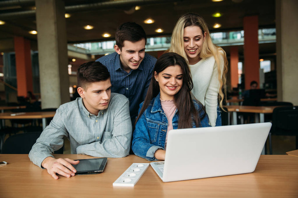 Groep van studenten studeren in de schoolbibliotheek, een meisje en een jongen zijn met behulp van een laptop en verbinding maken met internet - Foto, afbeelding