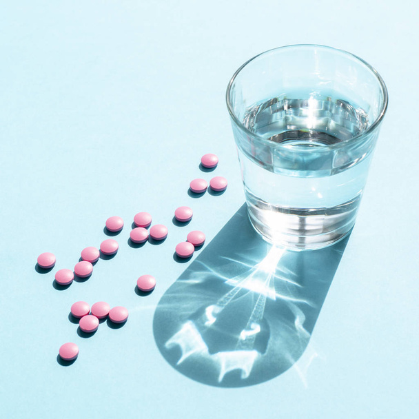 Water in glass Cup and pink round tablets on a blue surface - Фото, изображение
